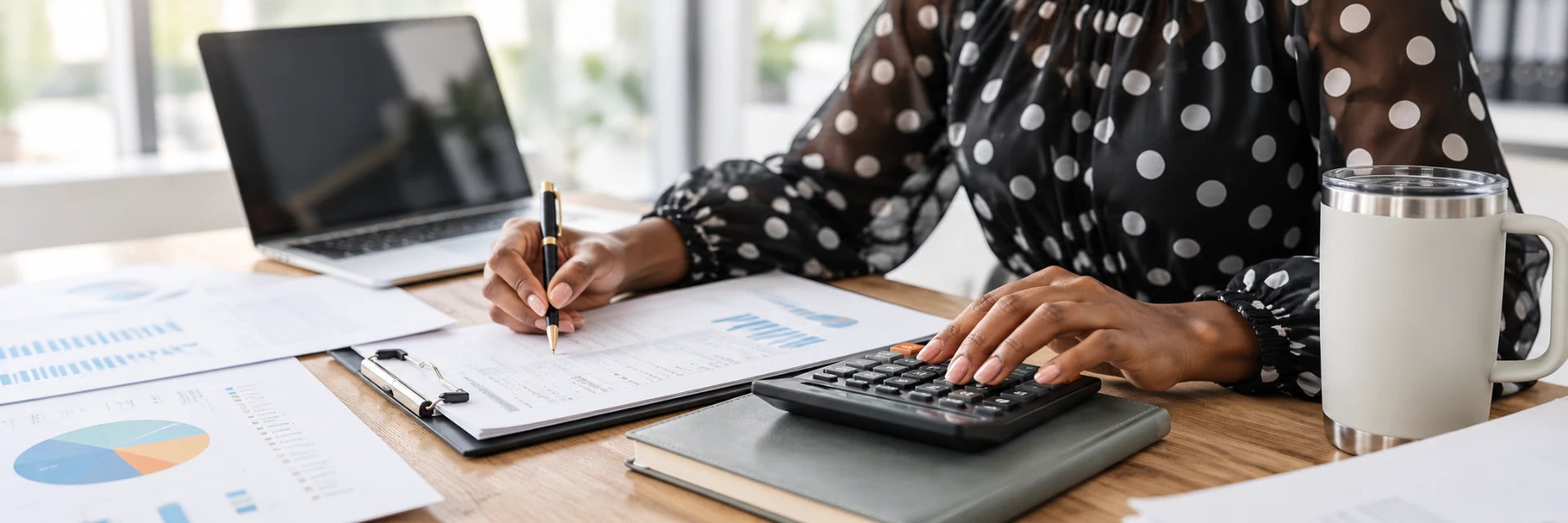 A bookkeeper working on financial reports at a desk with a laptop and calculator